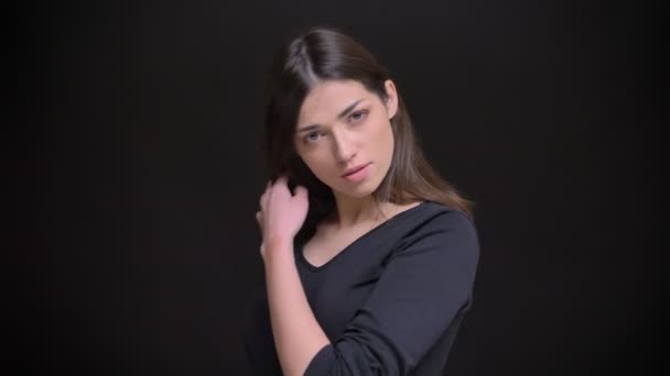 Porträtt av unga kaukasiska långhårig brunett flicka flirtingly skakar hennes hår in kameran på svart bakgrund. — Stockvideo