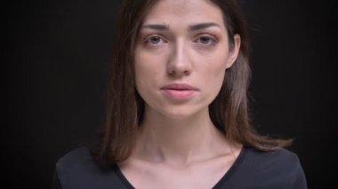 Yakın çekim portre Genç beyaz uzun saçlı esmer kız cidden içine kamera siyah arka plan üzerine izlerken.