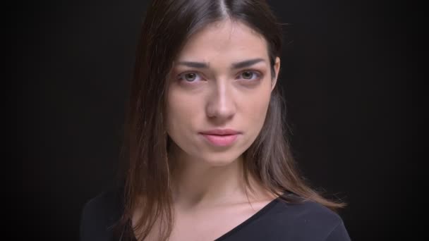 Detail portrét mladé kavkazské dlouhé vlasy brunetka zapne a sleduje klidně do kamery na černém pozadí. — Stock video