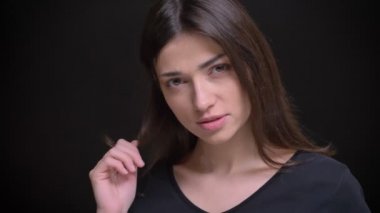 Yakın çekim portre Genç beyaz uzun saçlı esmer kız flirtingly üstünde parmak siyah arka plan üzerine saç büküm.