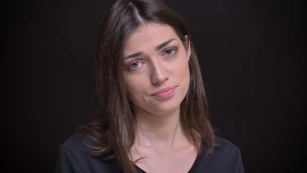 Detail portrét mladé kavkazské dlouhé vlasy brunetka stydlivě dívat do kamery na černém pozadí. — Stock video