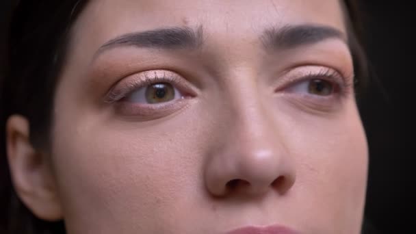 Närbild öga-porträtt i profil av unga kaukasiska långhårig brunett tjej tittar lugnt in kameran på svart bakgrund. — Stockvideo