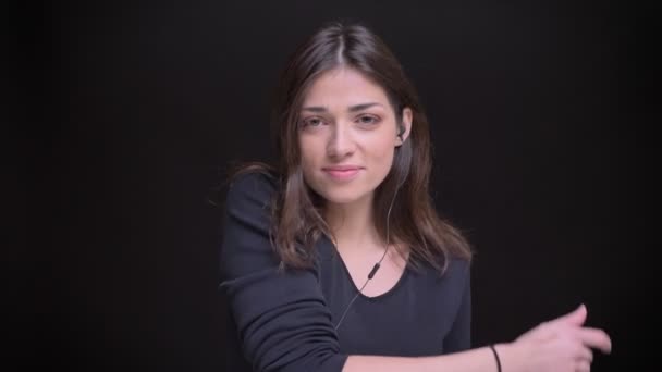 Portrét mladé kavkazské dlouhé vlasy brunetka v sluchátka radostně tančí na černém pozadí. — Stock video