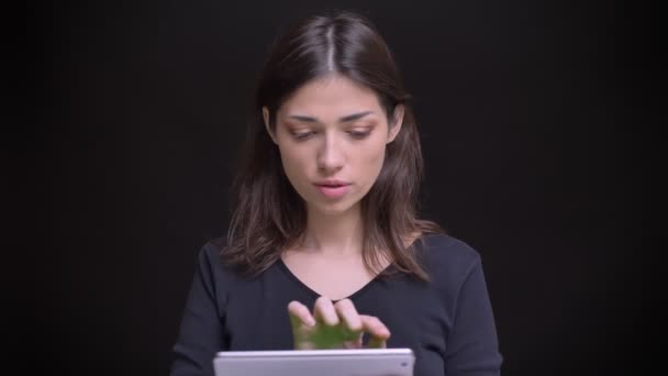 Bastante morena de pelo largo mirando en la tableta y muestra su pantalla verde horizontal en la cámara sobre fondo negro . — Vídeo de stock