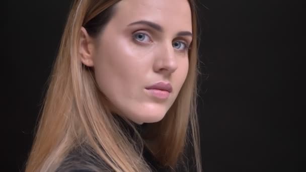 Close-up portret van de jonge Kaukasische langharige blonde meisje draait met camera en horloges serieus op zwarte achtergrond. — Stockvideo