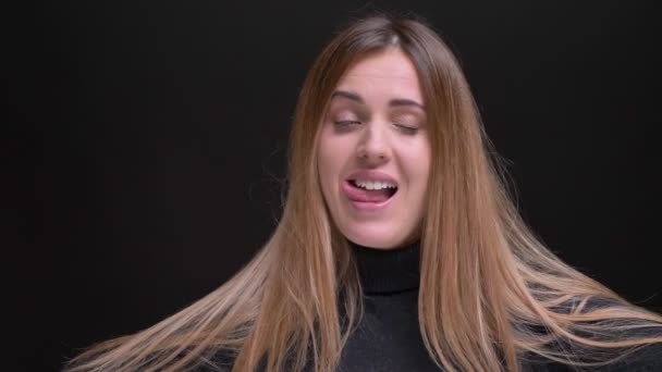 Portret van de jonge Kaukasische langharige blonde meisje vreugdevol vreemde gezichten maken en tonen van tong op zwarte achtergrond. — Stockvideo