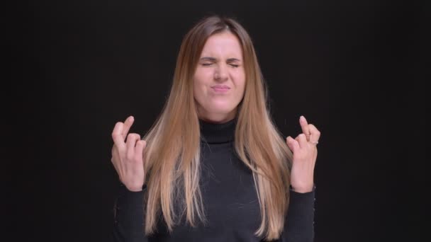 Portrait of caucasian long-haired blonde girl joyfully gesturing crossed-fingers sign to show hope on black background. — Stock Video