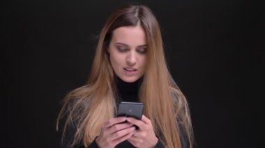 Uzun saçlı sarışın kız gülümseyerek smartphone izliyor ve kamera siyah arka plan üzerine gözlerini yükselterek genç portresi.