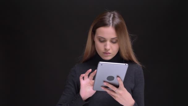 Retrato de una joven rubia caucásica de pelo largo observando atentamente en la tableta sobre fondo negro . — Vídeo de stock