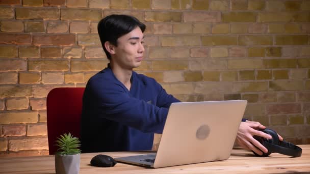 Kulaklıklar koyarak ve video aramasý laptop sahip genç çekici Kore erkek öğrenci portresi portre — Stok video