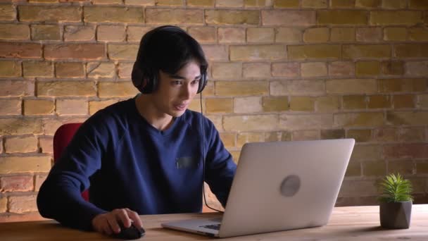 Крупним планом портрет молодий привабливою Корейська учень в навушниках, маючи Відеодзвінок ноутбук і жестикулюючи — стокове відео