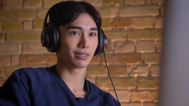 Primer plano retrato de joven atractivo hombre coreano en auriculares jugando videojuegos en interiores — Vídeo de stock