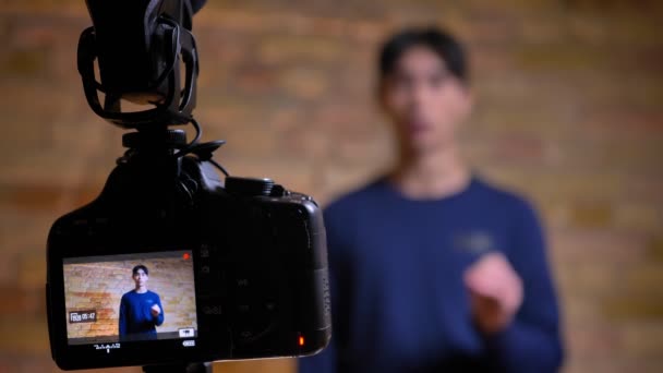 Primer plano centrado rodaje de la cámara de grabación joven coreano videoblogger masculino hablando y gesticulando reenfoque en el altavoz — Vídeos de Stock