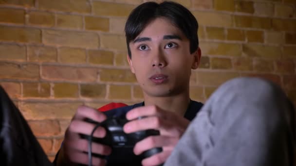 Close-up para baixo retrato de jovem coreano masculino jogar videogames e ser animado dentro de casa — Vídeo de Stock