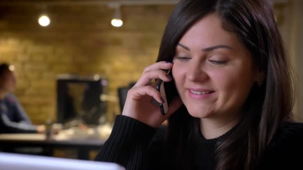 Close-up de adulto feliz mulher de negócios caucasiana falando ao telefone e sorrindo alegremente enquanto se senta na frente do laptop — Vídeo de Stock