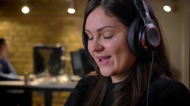 Portret zbliżenie dorosły kaukaski kobieta brunetka wesoło słuchanie muzyki w słuchawkach i śpiewania na miejscu pracy — Wideo stockowe