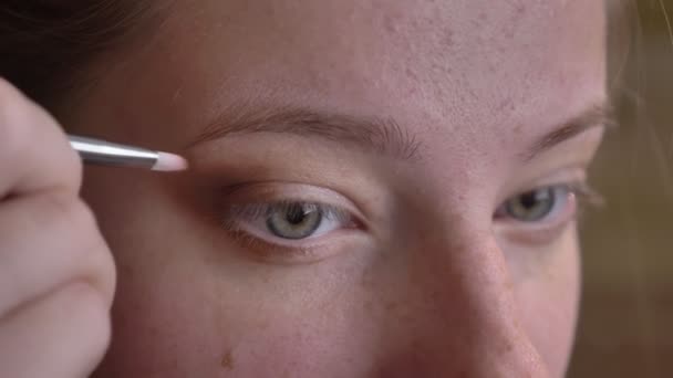 Retrato de close-up de jovem artista de maquiagem feminina caucasiana aplicando sombras castanhas com uma escova — Vídeo de Stock