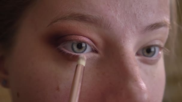 Closeup portret van de jonge Kaukasische vrouwelijke make-up artiest toepassing van witte eyeshadows met een borstel — Stockvideo