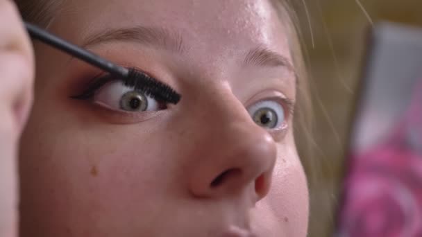 Retrato de close-up de uma jovem maquiadora caucasiana aplicando um rímel preto em sua pálpebra superior — Vídeo de Stock