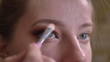 Çarpıcı üzerinde kahverengi kaş dumanlı gözler göz altında beyaz eyedhadows uygulayarak genç beyaz kadın makyaj sanatçısı closeup portresi