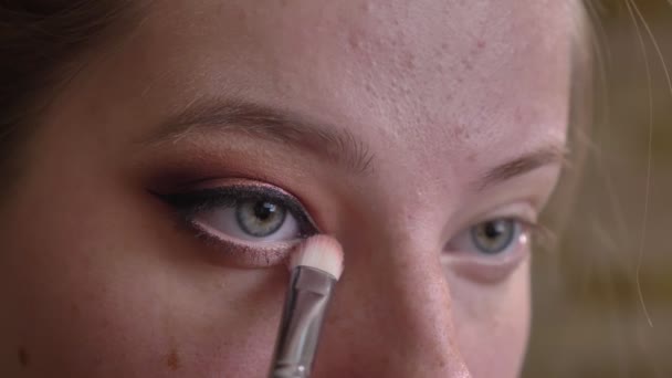 Närbild porträtt av unga kaukasiska kvinnliga makeupartist tillämpa vit ögonskuggor till ögat hörn — Stockvideo