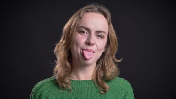 Крупним планом портрет дорослої білої жінки дивиться на камеру і показує язик — стокове відео