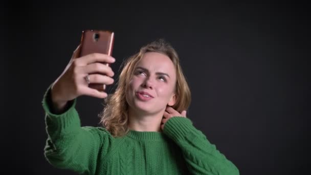 Closeup portrait of adult caucasian female having a video call on the phone and fixing her hair in front of the camera — Stock Video