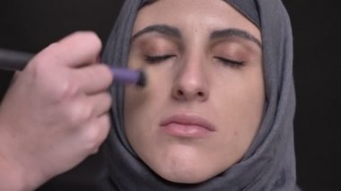 Yakın çekim portre siyah arka plan üzerine hijab orta yaşlı Müslüman kadın için makyaj yapıyor eller.