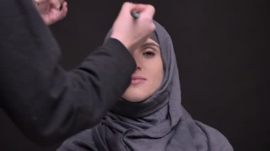 Türban kapalı gözler siyah arka plan ile orta yaşlı Müslüman kadın için makyaj yapıyor eller portresi.