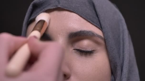 Close-up oog-portret van vrouwelijke handen doet make-up voor middelbare leeftijd Moslimvrouw in hijab op zwarte achtergrond. — Stockvideo