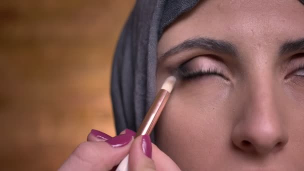 Närbild halv-porträtt av kvinnliga händer gör ögonmakeup med borste för muslimsk kvinna i hijab på bricken vägg bakgrund. — Stockvideo