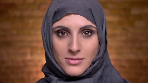 Portrait de femme musulmane en hijab avec un maquillage lumineux regardant calmement dans la caméra sur fond de mur de poulet . — Video