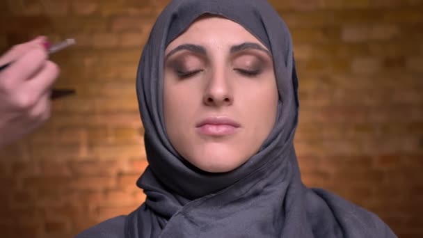 Portret van vrouwelijke handen doen oog make-up met behulp van bruin pensil voor de moslimvrouw in hijab op bricken muur achtergrond. — Stockvideo