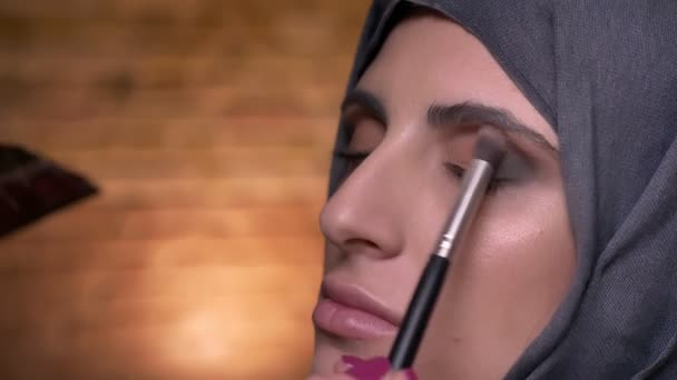 Porträt weiblicher Hände beim Make-up mit kleinem Pinsel für muslimische Frau im Hijab auf gemauertem Hintergrund. — Stockvideo