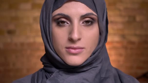 Portrait de belle femme musulmane en hijab avec maquillage lumineux regardant avec sourire dans la caméra sur fond de mur de poulet . — Video