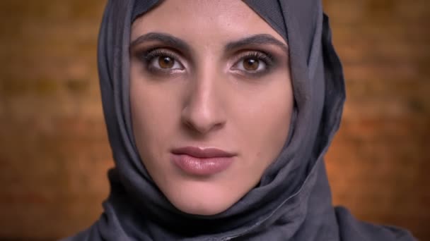 严重中年穆斯林妇女的肖像在头巾与明亮的化妆平静地看着相机在砖墙背景 — 图库视频影像
