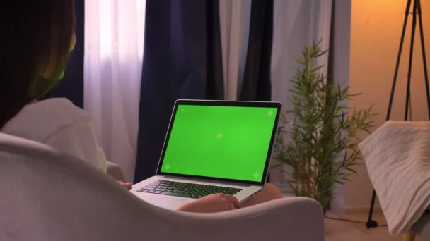 Крупный план заднего вида молодой белой женщины с помощью ноутбука с зеленым хроматическим экраном в уютном доме в помещении — стоковое видео