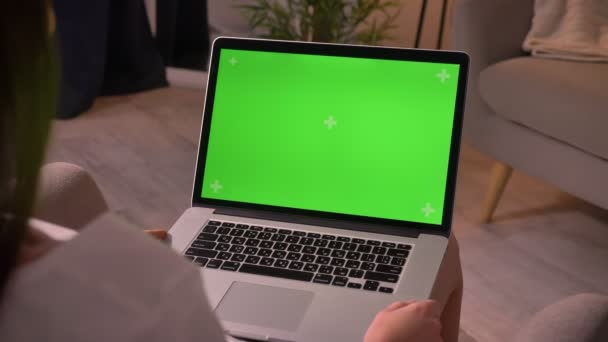 Крупним планом задній перегляд зйомки молодої білої жінки, що тримає ноутбук з зеленим екраном з хромовим ключем в хомі в приміщенні — стокове відео