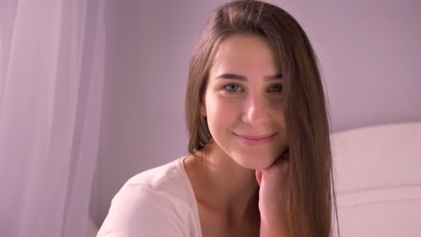 Gros plan portrait de jeune belle brune femelle regardant caméra et souriant dans la chambre à coucher à l'intérieur de la maison — Video