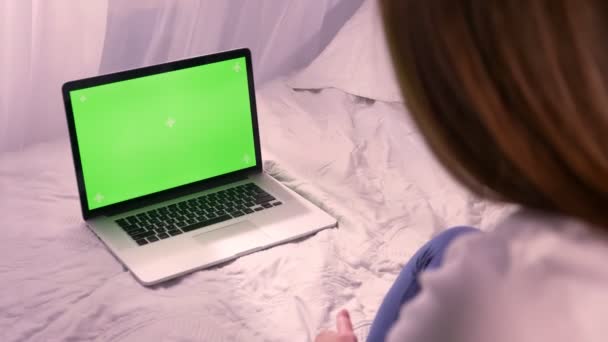 Close-up visão traseira da jovem morena olhando para a tela verde chroma-key do laptop sentado na cama em casa dentro de casa — Vídeo de Stock