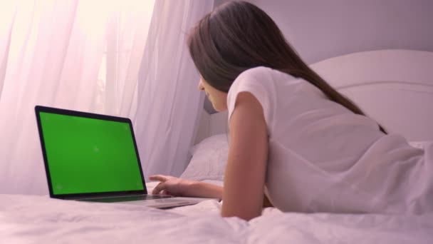 Close-up visão traseira do jovem caucasiano atraente enviando uma mensagem no laptop com tela verde chroma-key deitado na cama — Vídeo de Stock