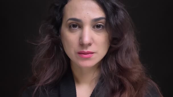 Портрет крупным планом взрослого привлекательного кавказского женского лица с карими глазами, смотрящего прямо в камеру на фоне изолированного на черном фоне — стоковое видео
