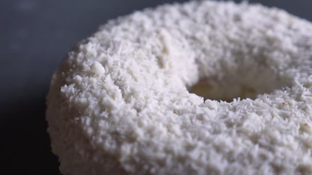 Close-up half-shot of tasty white donut with coconut chips spinning slowly on gray table background. — Stock Video