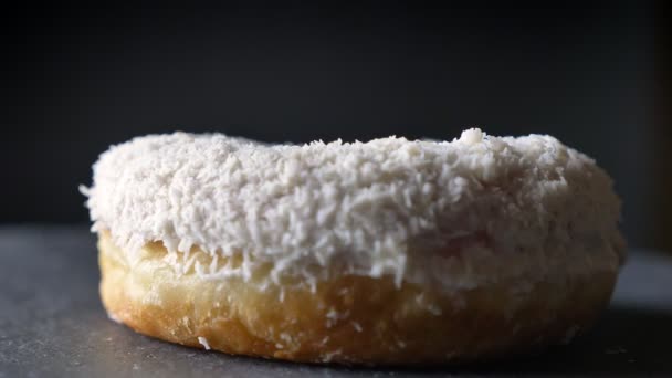 Close-up circling around shot of tasty white donut with coconut chips spinning slow on gray table background . — Stok Video