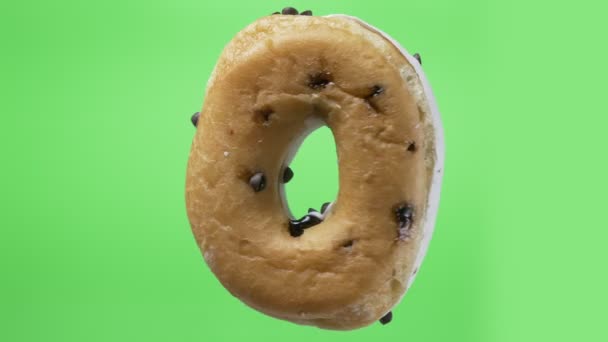 Shot of delicious white donut with chocolate chips spinning around on green background. — Stock Video