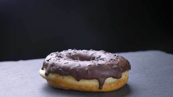 Close-up circling around shot of delicious glazed brown donut with chocolate chips spinning slowly on gray table background. — Stock Video
