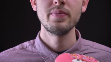 Yakın çekim portre lezzetli gösterilen adamın çok renkli cips ve gözleri siyah arka plan üzerine pembe çörek sırlı.