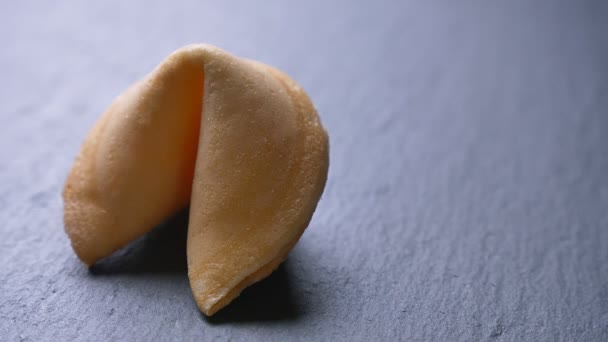 Close-up circling around shot of fortune cookie spinning slowly on gray table background. — Stock Video