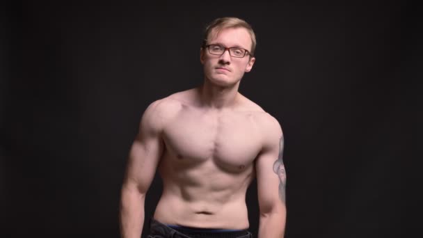 Porträt eines nackten jungen, muskulösen Mannes mit Brille, der glücklich seinen Bizeps in die Kamera auf schwarzem Hintergrund zeigt. — Stockvideo