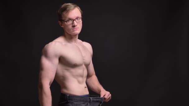 Portrait de profil de jeune homme musclé nu dans des lunettes montrant volontiers les résultats de la perte de poids dans l'appareil photo sur fond noir . — Video